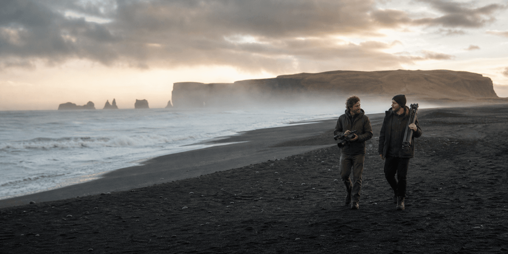 Two filmmakers walking along a black-sand coast